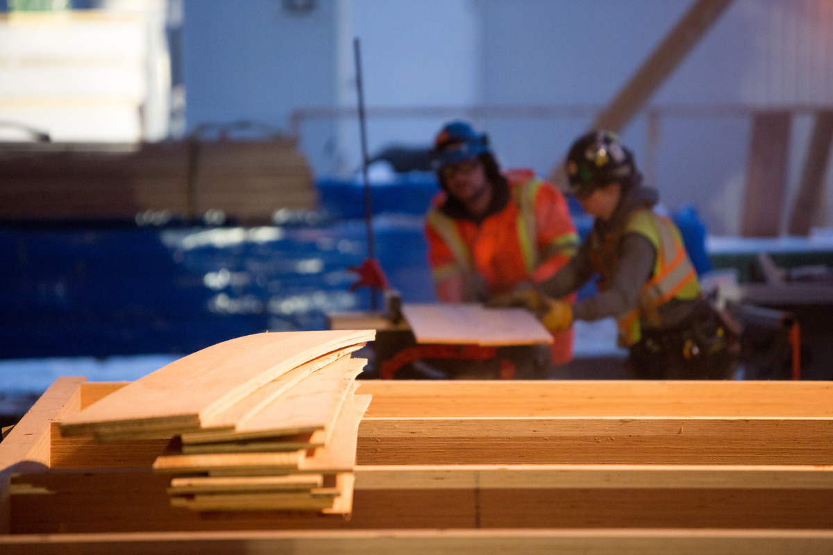 Stack of completed laminated slats, with workers in the background at this mass timber construction site, that demonstrate the value, versatility and flexibility of light-frame wood and mass timber construction and design